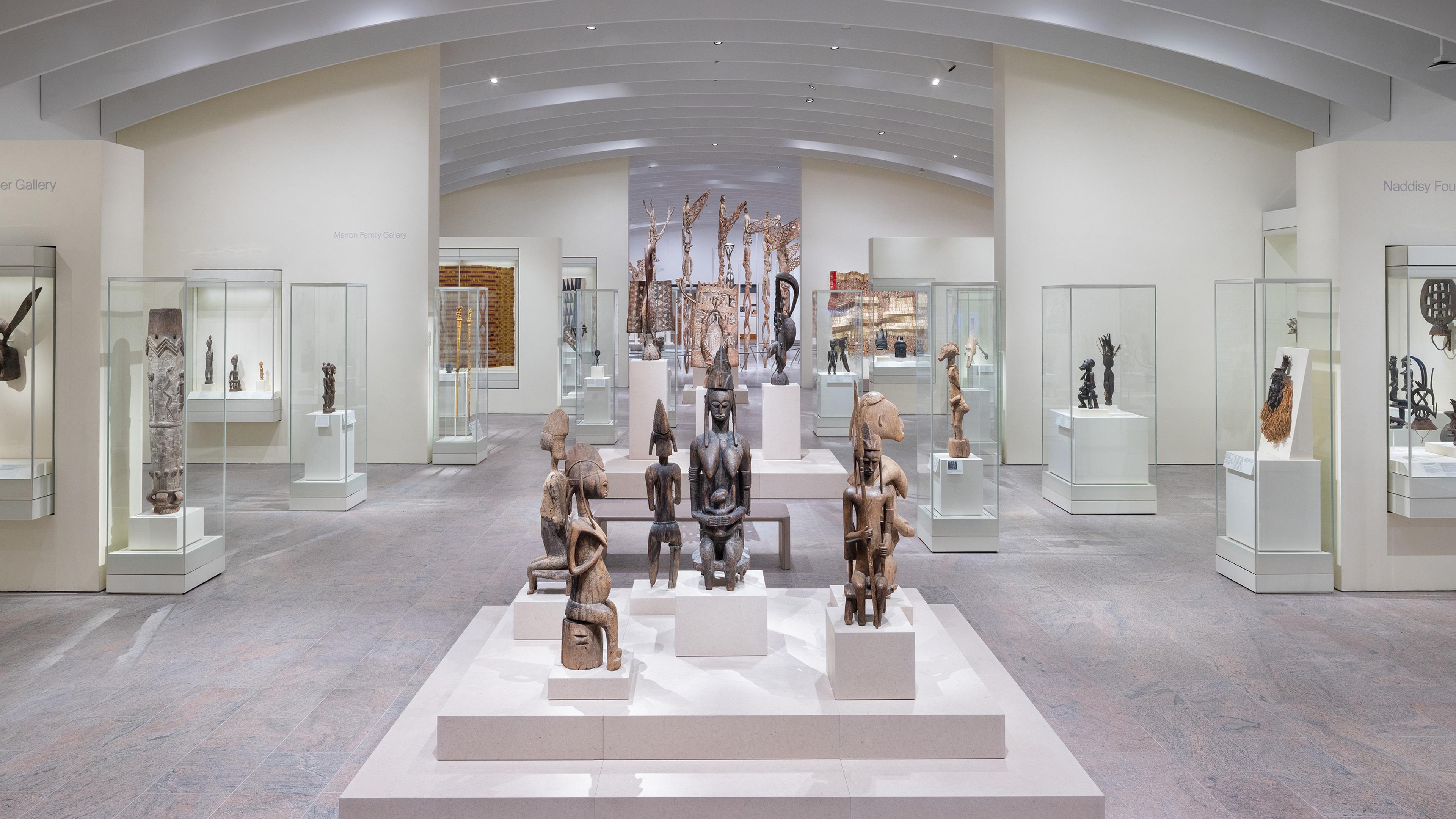 A platform of wooden sculptures surrounded by glass cases under a vaulted ceiling