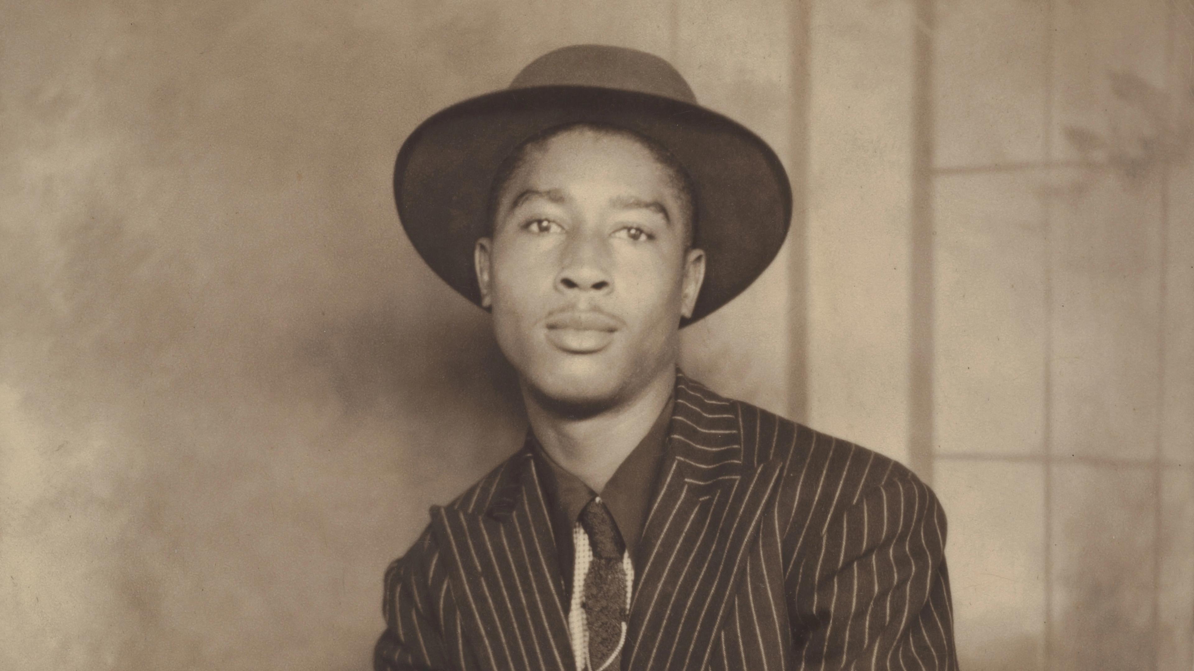 Cropped studio portrait of a man in a pinstripe suit, tie, and hat