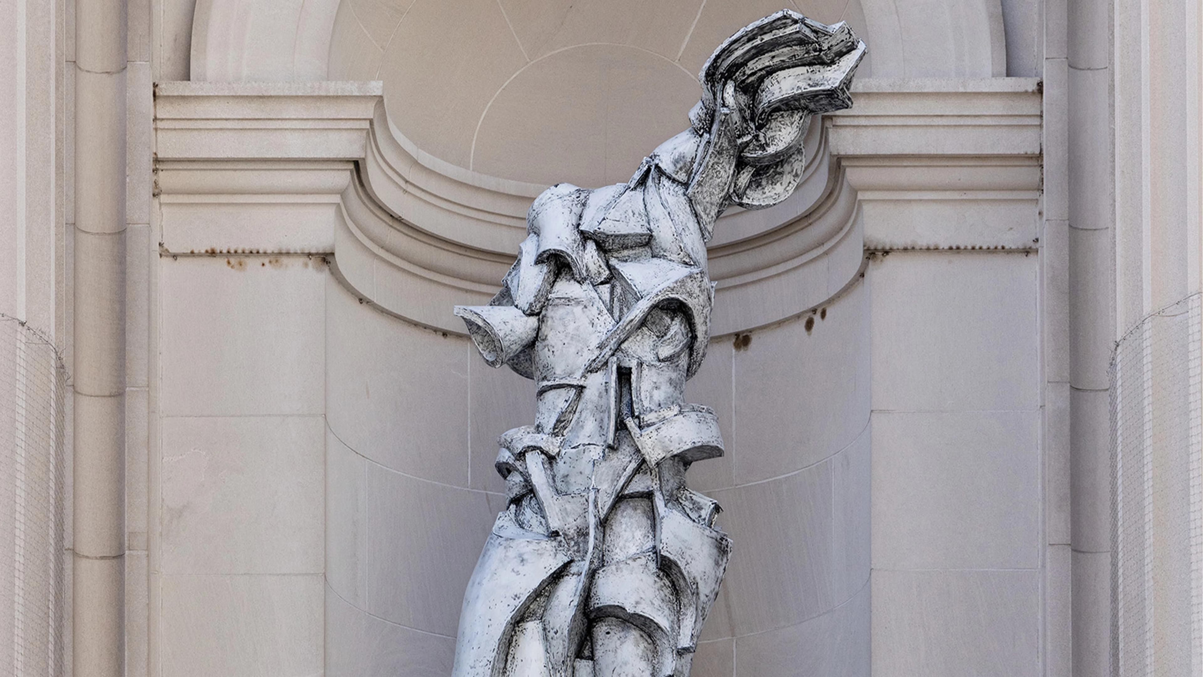 Futuristic sculpture of a fragmented, abstract human form in stone against a neoclassical arch. The tone is dynamic and modern amidst classical architecture.