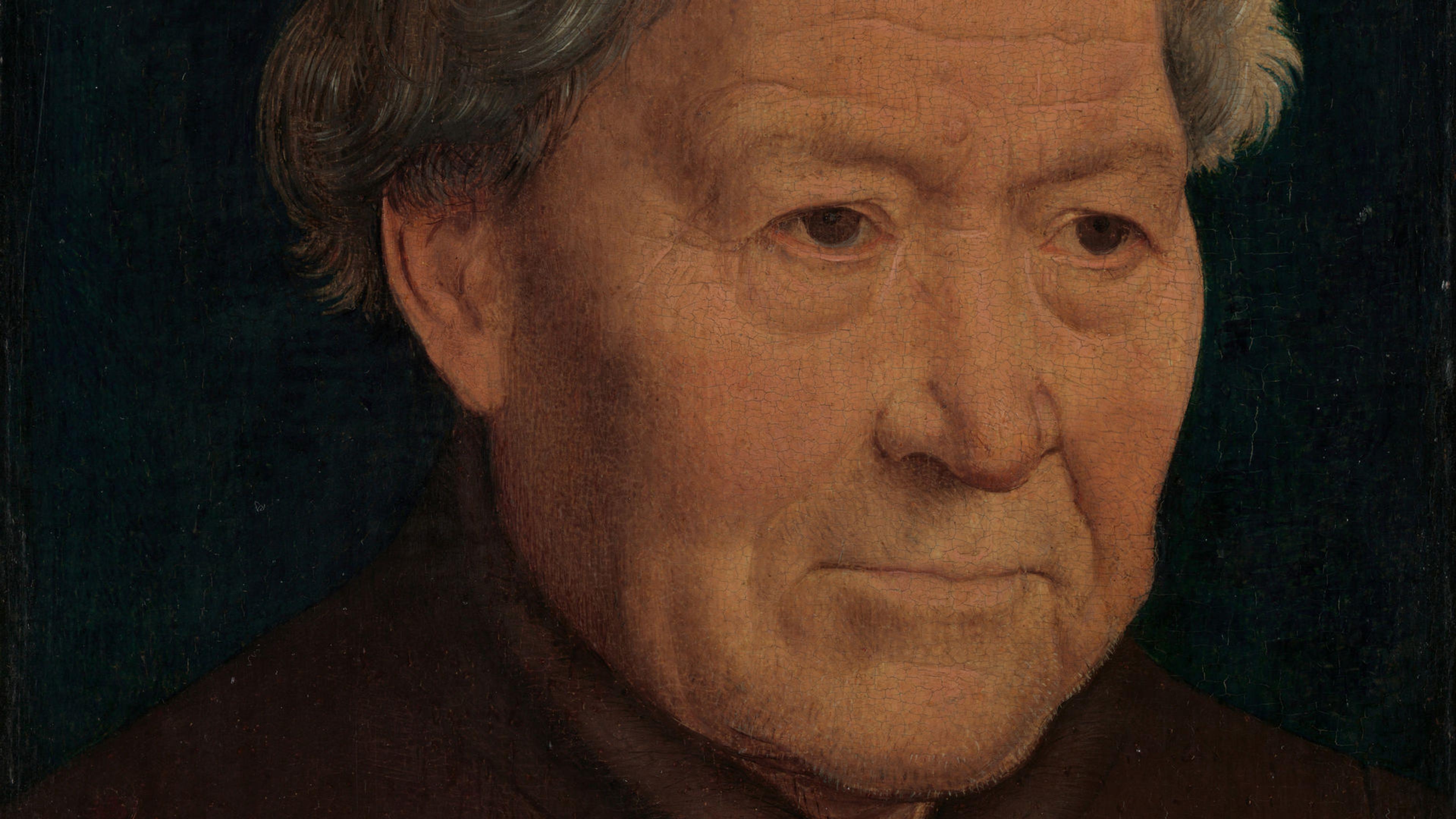 Portrait of an old man in a simple brown tunic with fur trim. His hands are placed over each other in the bottom right corner of the frame.