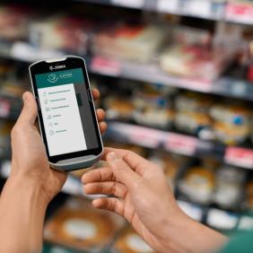 a person is holding a zebra barcode scanner in their hands in a grocery store .