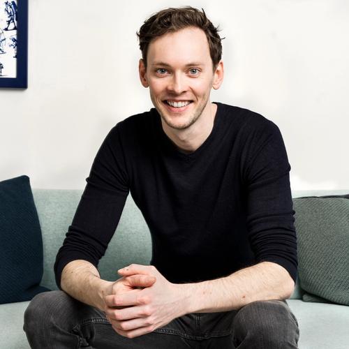 a man is sitting on a couch with his hands folded and smiling .