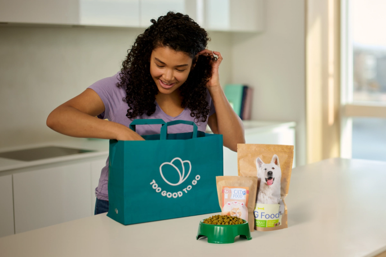 a woman talking on a cell phone next to a bag that says too good to go